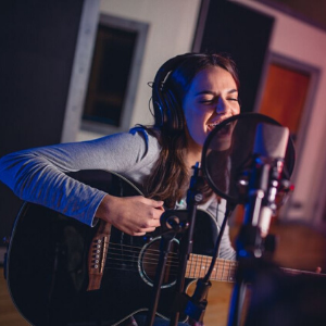 female singer recording in the studio with guitar and microphone